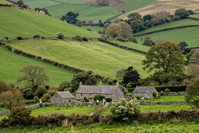 Rolling green countryside valley with a clustered stone cottage and outbuildings divided by dry stone hedgerows