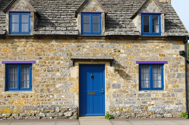 Front facade of a traditional English stone cottage with bright blue door and window frames