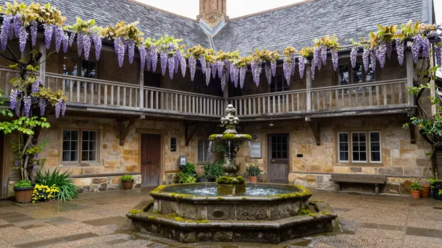 Old stone inn courtyard with a mossy fountain, wisteria draped wooden galleries in soft spring rain