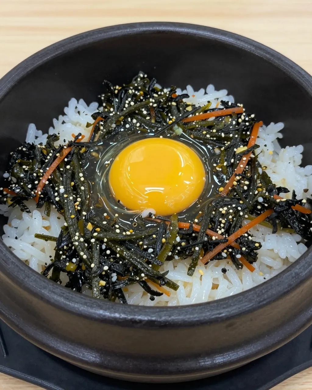 Close-up of sizzling dolsot bibimbap topped with raw egg yolk, seaweed, carrot strips and sesame seeds in a black stone bowl