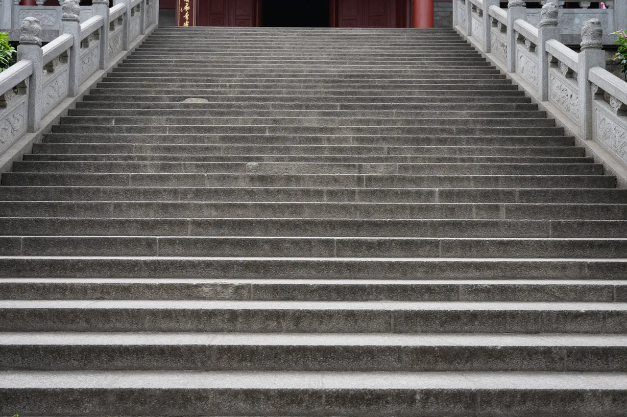 Wide weathered stone steps lead upward to the entrance of a traditional East Asian temple flanked by carved railings