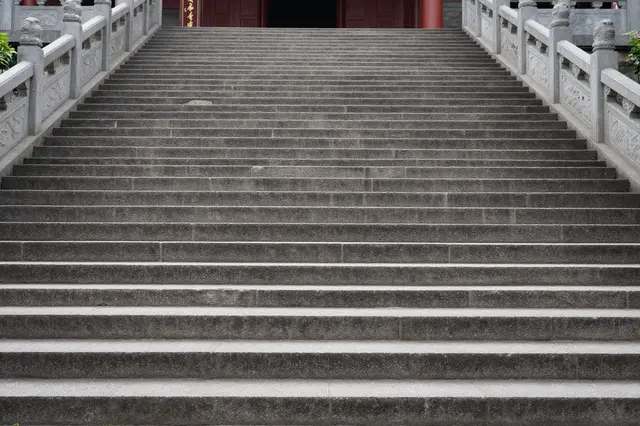 Wide weathered stone steps lead upward to the entrance of a traditional East Asian temple flanked by carved railings