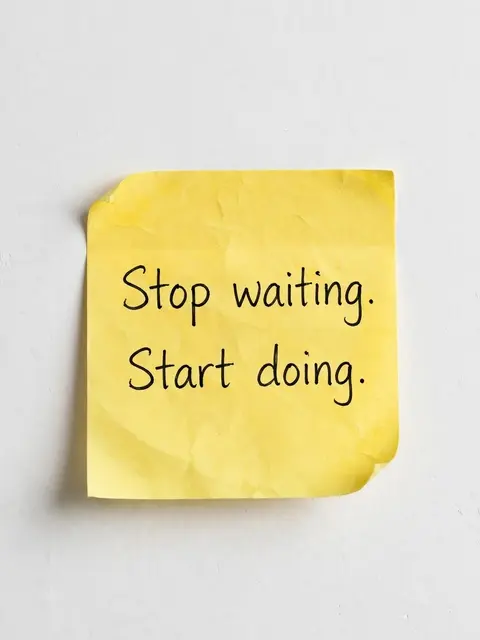 A crumpled yellow sticky note on a white wall displays the handwritten quote "Stop waiting. Start doing."