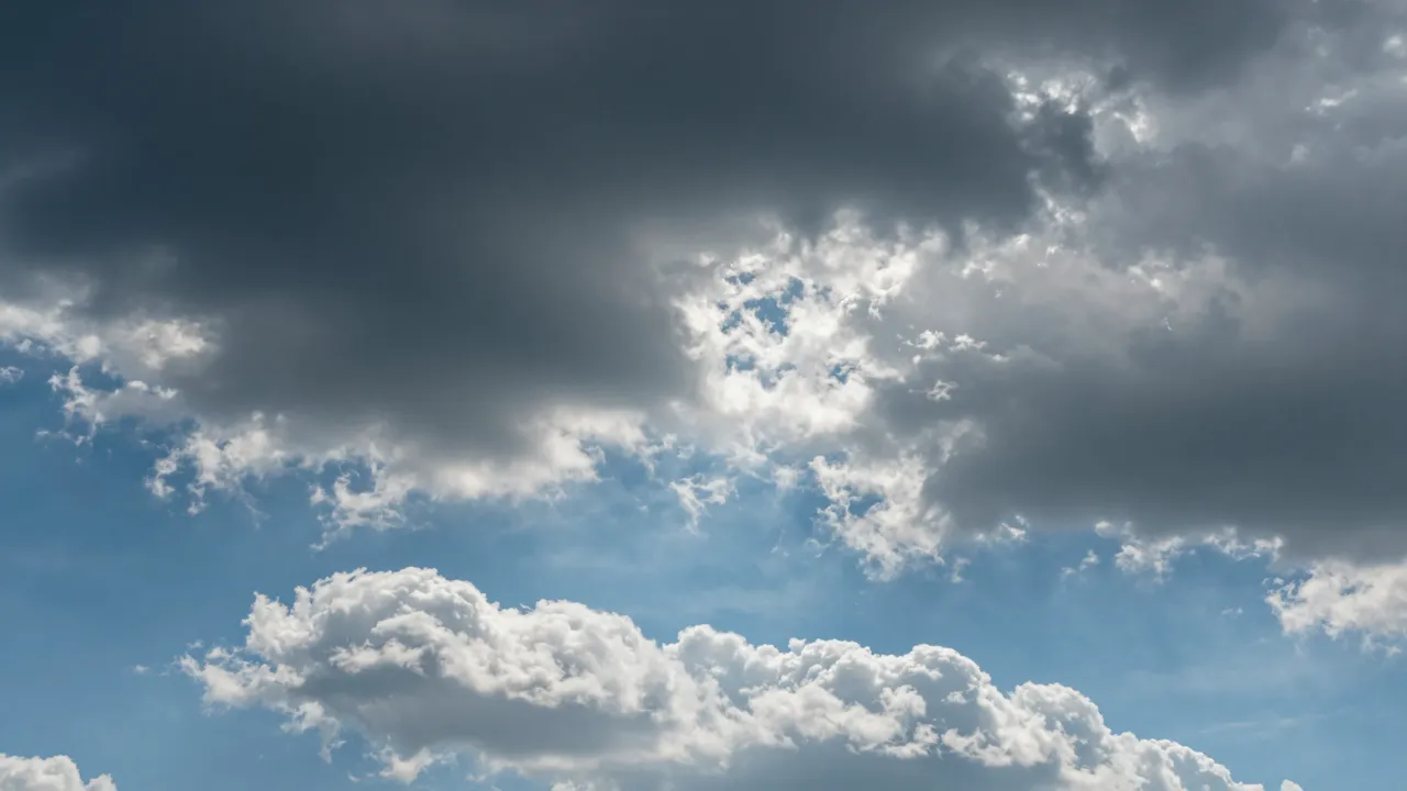 Dark storm clouds pull apart to reveal bright white fluffy clouds and clear patches of blue sky