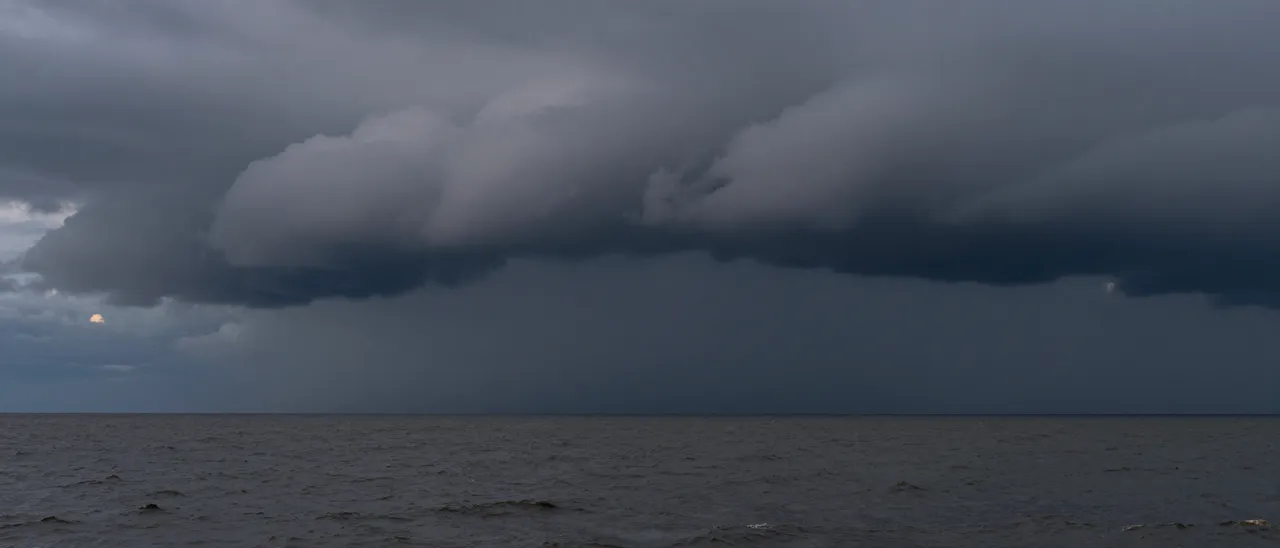 Dark shelf storm clouds roll over a choppy gray sea at dim dusk with a shadowed horizon