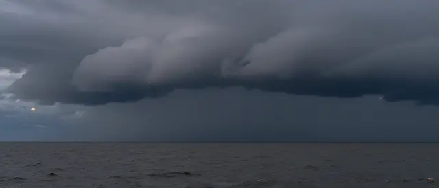 Dark shelf storm clouds roll over a choppy gray sea at dim dusk with a shadowed horizon