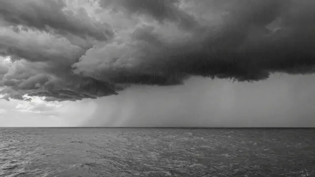 Black and white view of heavy rain curtains falling from dark squall clouds over a calm sea