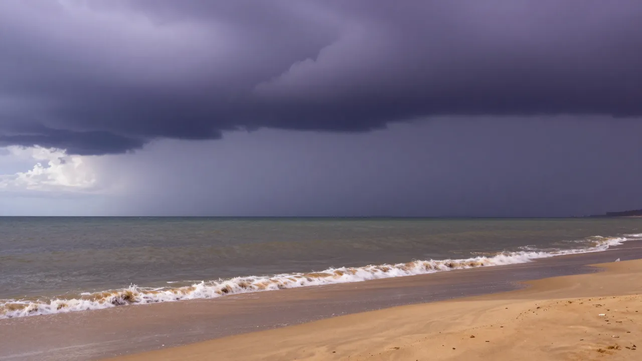 Dark purple storm clouds hang over a calm sea where small waves lap onto a sandy shore
