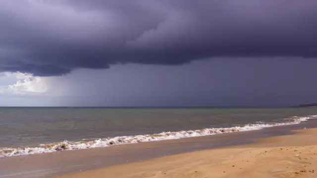 Dark purple storm clouds hang over a calm sea where small waves lap onto a sandy shore