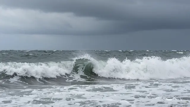 Turbulent crashing ocean waves roll beneath heavy dark overcast storm clouds