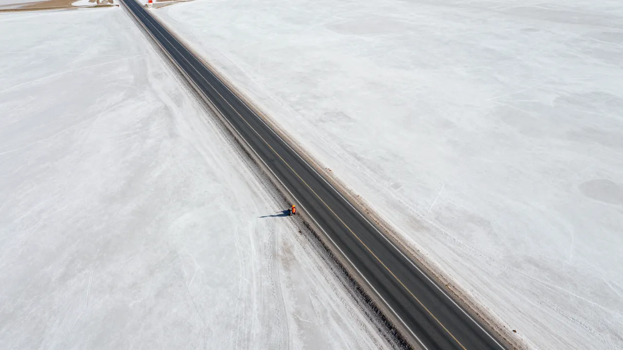 Aerial view of a long straight paved road cutting through an expansive bright white salt flat