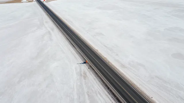Aerial view of a long straight paved road cutting through an expansive bright white salt flat