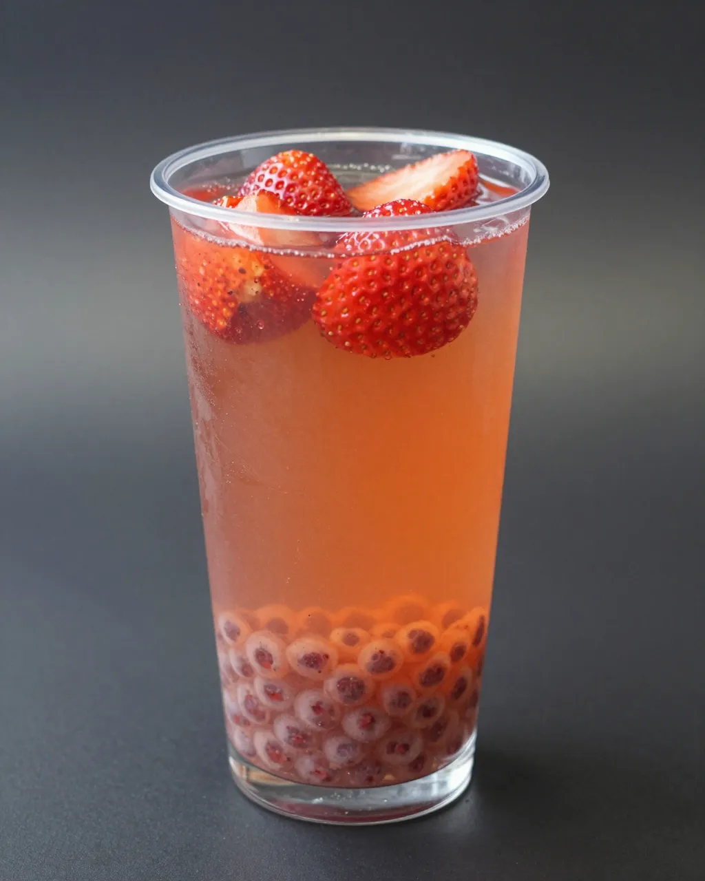 Clear plastic cup of pink fruit tea topped with fresh strawberries and filled with popping pearls