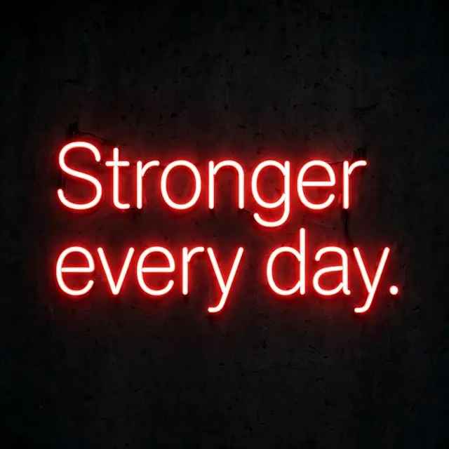Glowing red neon sign displaying the text "Stronger every day." mounted on a dark textured wall