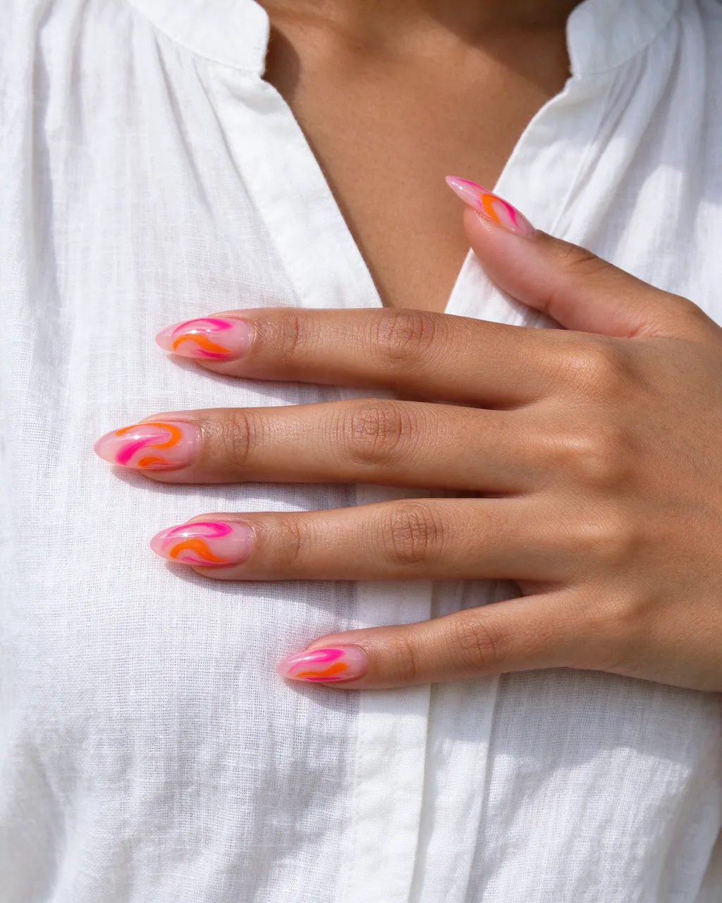 A Pacific Islander woman's hand with pink and orange swirl almond nails rests on a white linen shirt