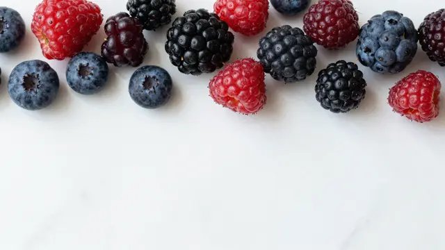 Mixed fresh summer berries arranged along the top edge of a light white marble surface with empty copy space below.
