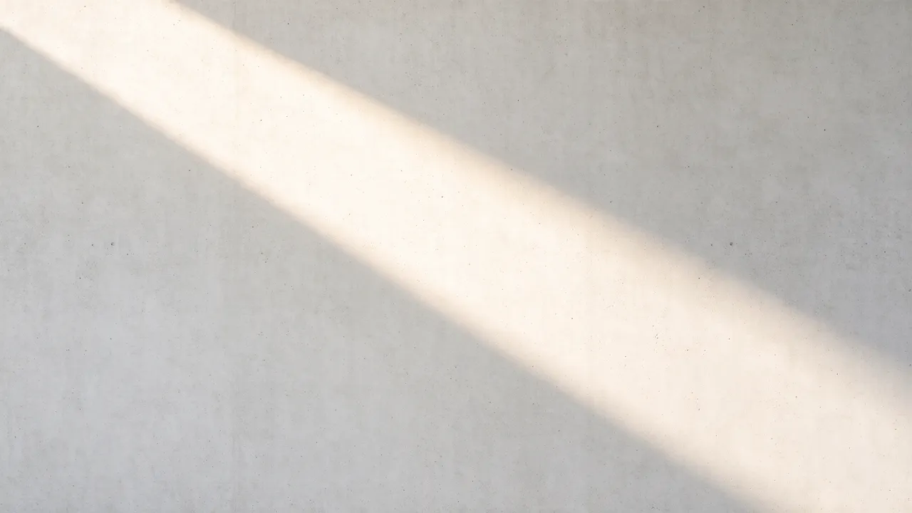 A soft diagonal beam of warm sunlight stretches across a smooth pale gray concrete wall