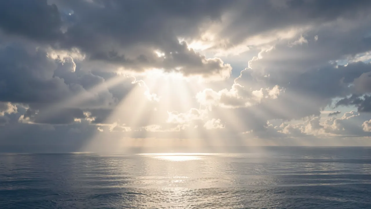 Bright sunbeams break through storm clouds to shine across a calm reflective sea