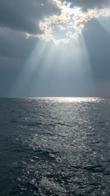 Sunbeams break through cloudy sky to shine on rippling open ocean surface