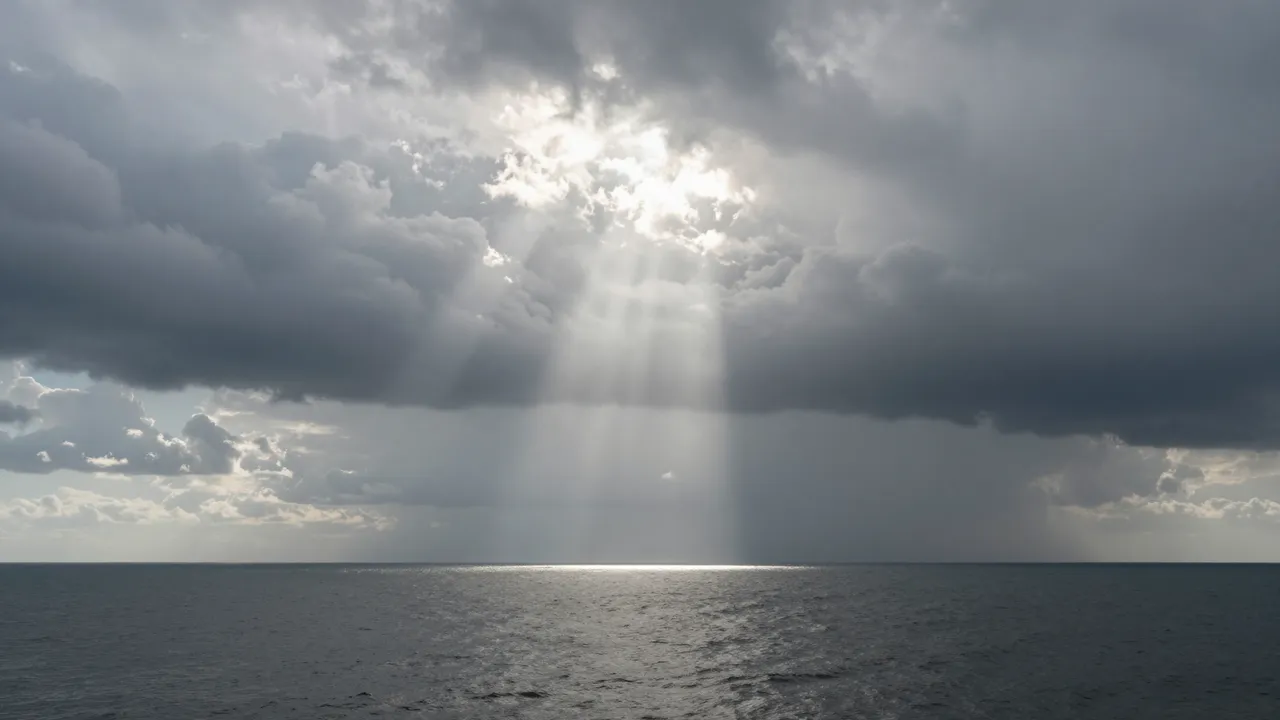 Bright shafts of sunlight break through storm clouds to fall across the surface of a calm dark sea