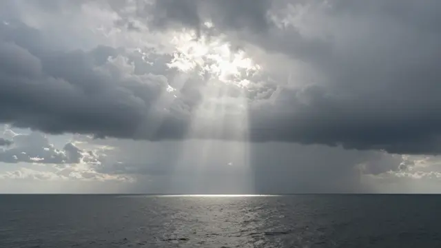 Bright shafts of sunlight break through storm clouds to fall across the surface of a calm dark sea