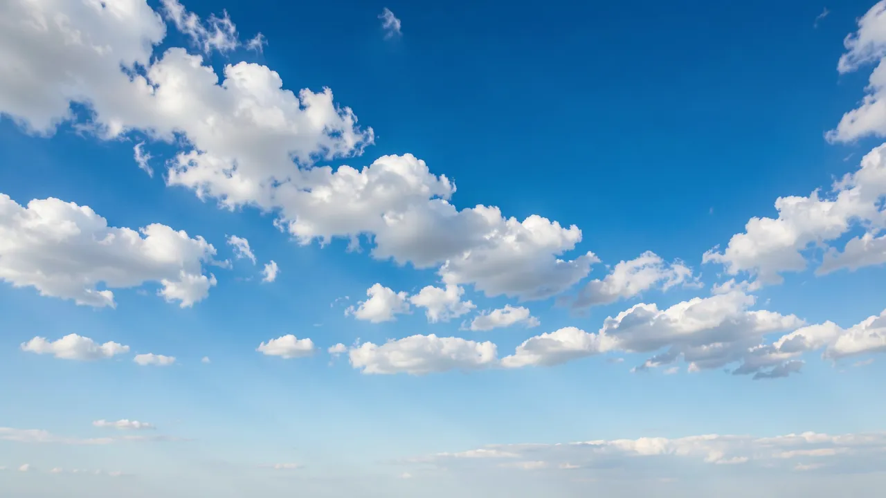 Bright clear blue sky dotted with sunlit fluffy white clouds and open empty space below.