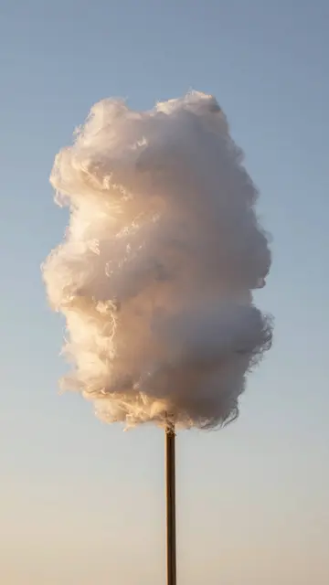 Fluffy cotton candy on a wooden stick is backlit by warm sunset light against a soft gradient sky