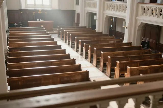 High angle view from a church balcony looking down onto empty wooden pews and a hazy sunlit nave
