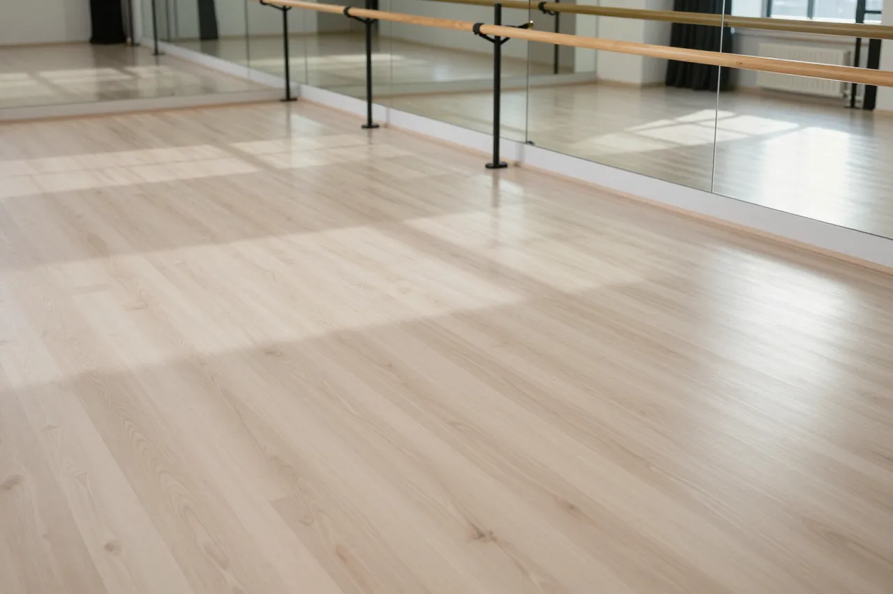 Empty bright dance studio with pale wood flooring, wall mirrors, and ballet barres lit by morning sunlight