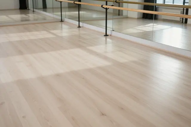 Empty bright dance studio with pale wood flooring, wall mirrors, and ballet barres lit by morning sunlight
