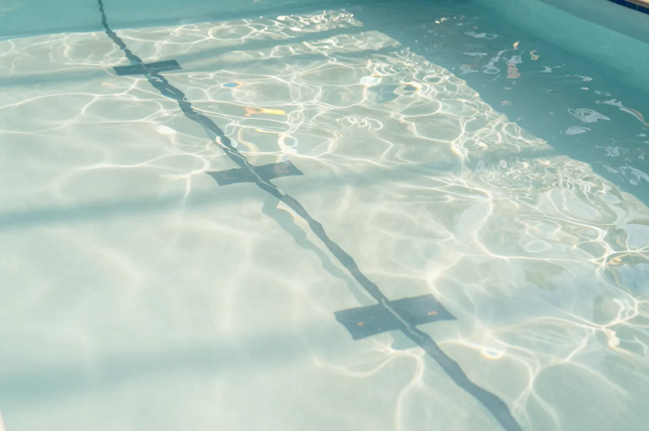 Rippled sunlight patterns cover the pale bottom of an empty outdoor swimming pool with a lane line
