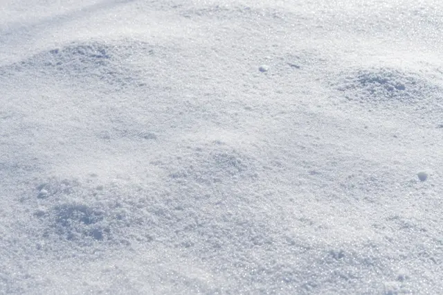 Sparkling fresh snow surface glistens under bright sunlight with soft subtle undulations