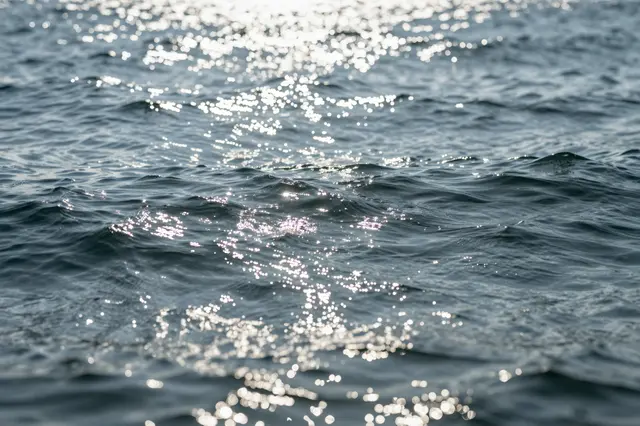 Bright sunlight glints and forms sparkling bokeh across gentle rippling blue ocean water.