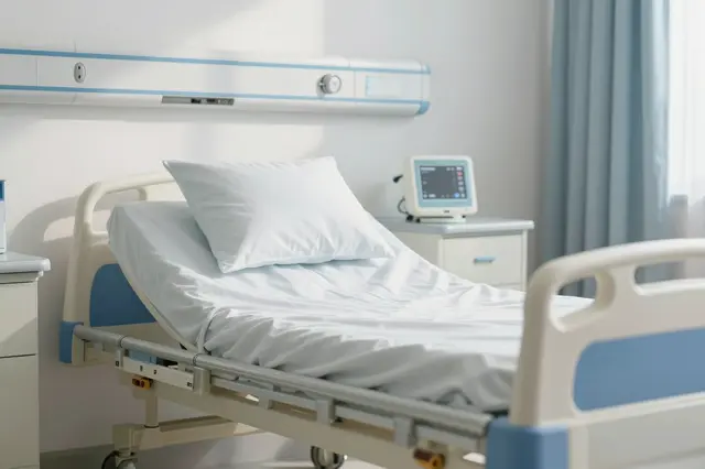 Empty adjustable hospital bed sits in a bright daylight hospital room with medical monitors and cabinetry