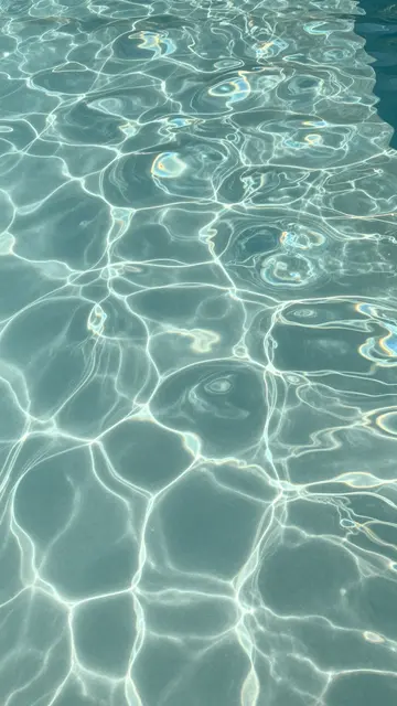 Top-down close-up of rippled sunlit turquoise swimming pool water with glowing caustic light patterns