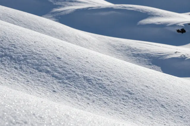 Glittering untouched powder snow covers smooth rolling hills in bright direct sunlight