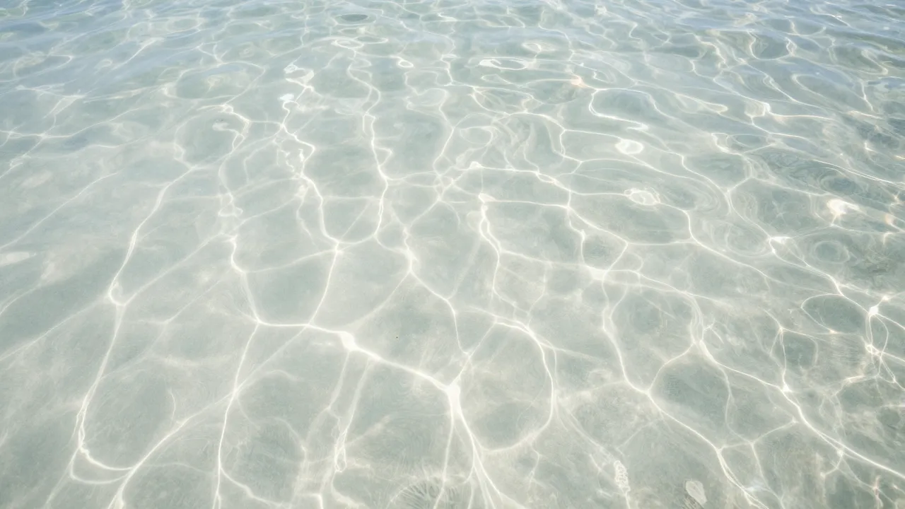 Overhead view of clear rippled tropical water with dancing sunlight patterns over pale sand