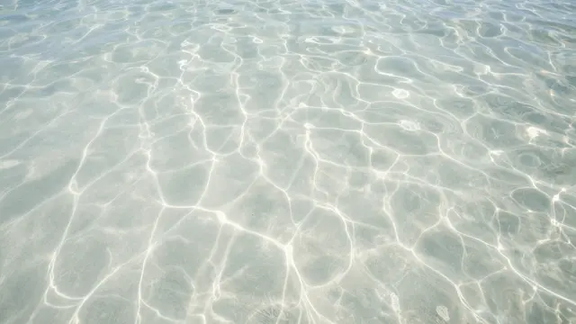 Overhead view of clear rippled tropical water with dancing sunlight patterns over pale sand