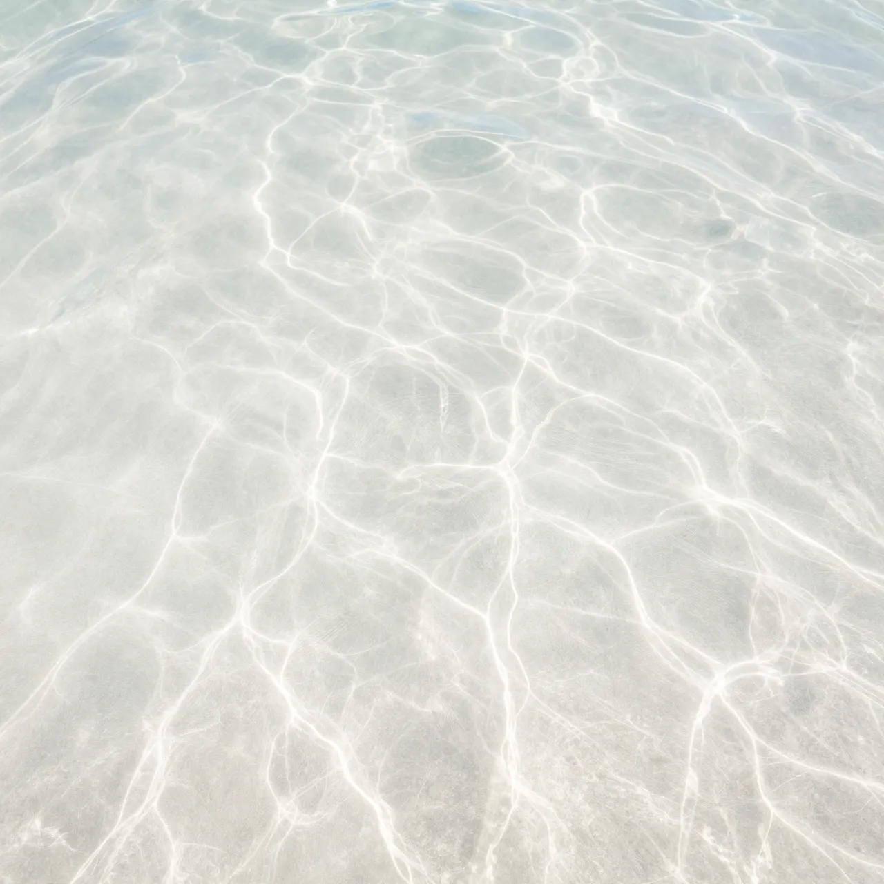 Wavy sunlit ripple patterns spread across bright white sand under clear shallow ocean water