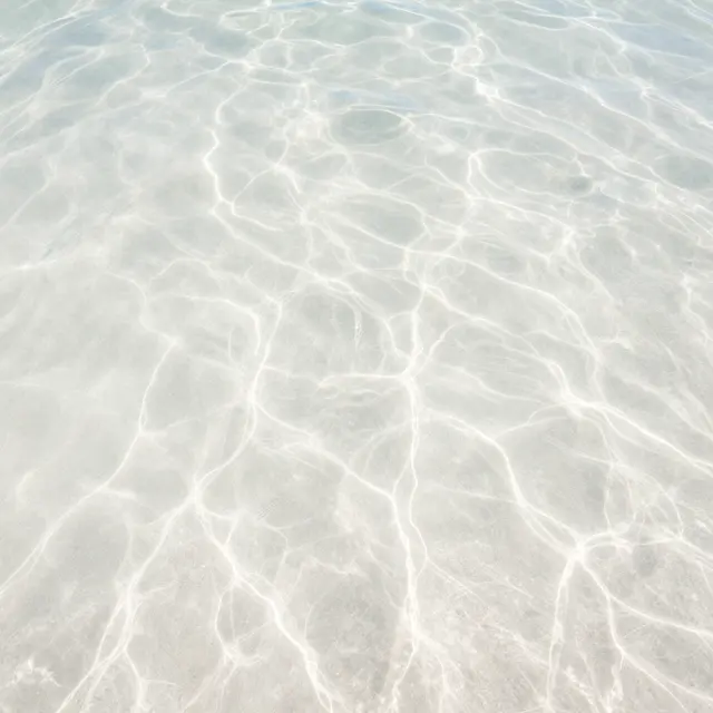 Wavy sunlit ripple patterns spread across bright white sand under clear shallow ocean water