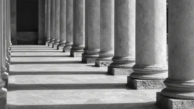 Black and white view of a lined stone colonnade with parallel shadow bands stretching across paving