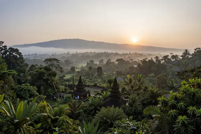 Warm sunrise light illuminates traditional temples nestled in a misty tropical jungle valley