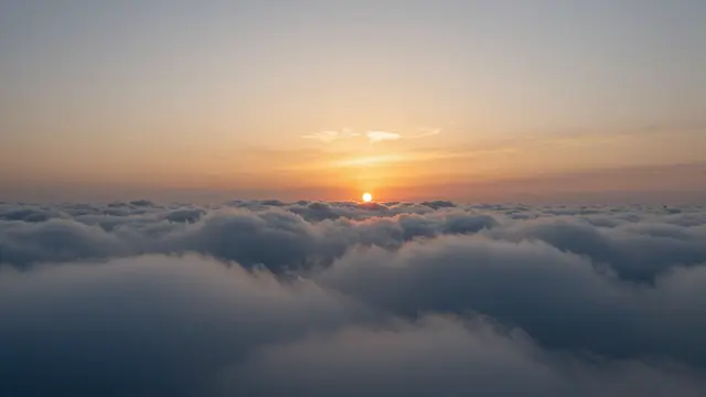 A high altitude view of a warm sunset sitting over a vast, rolling layer of clouds.