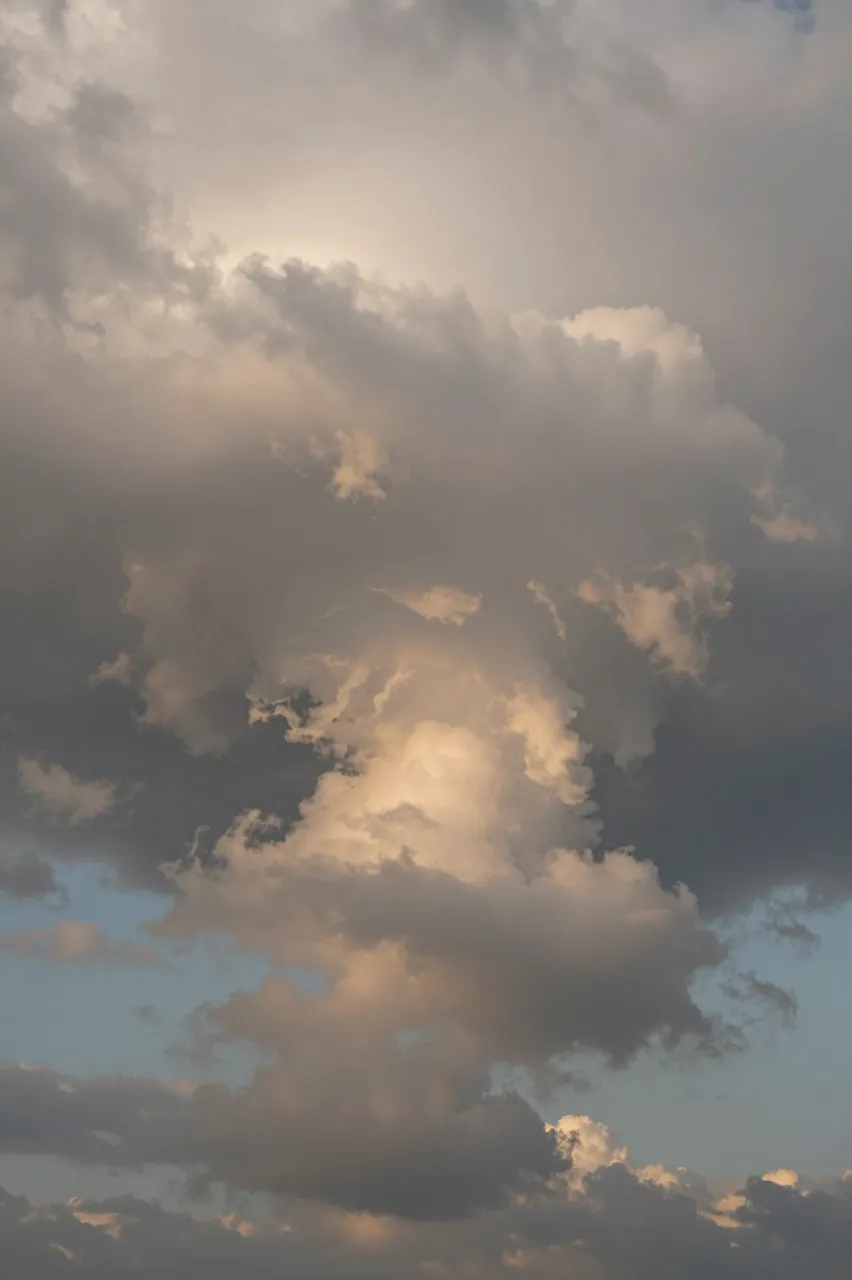 Towering storm clouds glow with warm golden light from the setting sun against patches of pale blue sky
