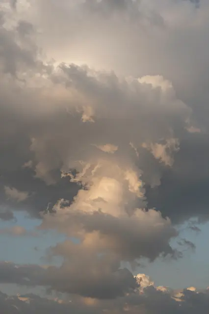 Towering storm clouds glow with warm golden light from the setting sun against patches of pale blue sky