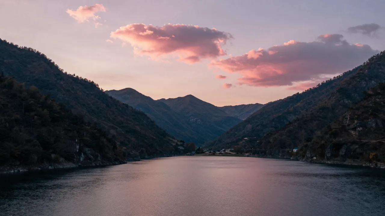 Calm mountain lake reflects pink sunset clouds framed by forested valley slopes
