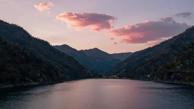 Calm mountain lake reflects pink sunset clouds framed by forested valley slopes