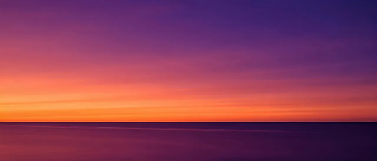 Smooth sunset gradient from tangerine orange to deep violet above a thin straight ocean horizon with calm reflective water.