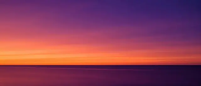 Smooth sunset gradient from tangerine orange to deep violet above a thin straight ocean horizon with calm reflective water.