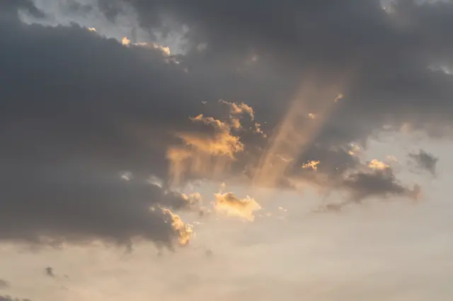 Golden sunbeams and virga streaks hang beneath dark storm clouds at warm sunset